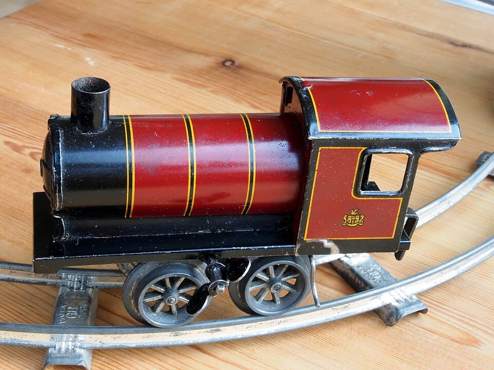 A vintage red and black wind-up toy train engine sitting on metal tracks.