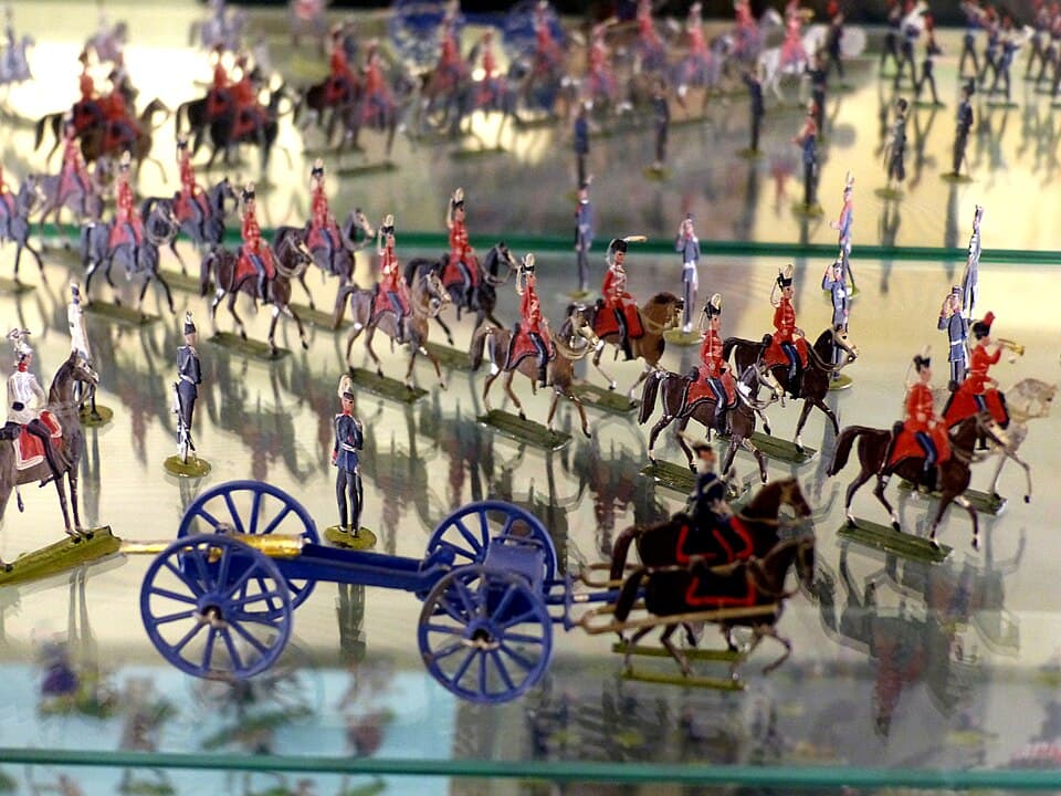 A collection of vintage toy metal soldiers and a blue artillery carriage on display.