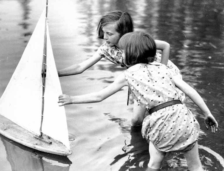 Children playing with a wooden toy sailboat